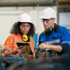 a man and woman wearing hard hats looking at a clipboard
