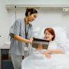 a nurse showing a tablet to a woman in a hospital bed