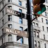 A traffic light in downtown NYC with the words Wall ST on the attached street signs.