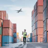 a man in a safety vest walking down a street with a plane flying above
