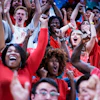 Ecstatic crowd sitting in the bleachers of a crowded sports stadium raise their hands up and cheer loudly during a professional soccer match as their favorite home football league takes the lead