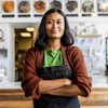 a woman in a apron standing in front of a bakery